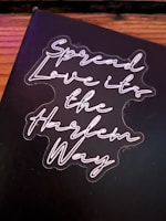 A black background with neon-style cursive text that reads 'Spread Love it's the Harlem Way'. The text is bright and stands out against the darker backdrop.