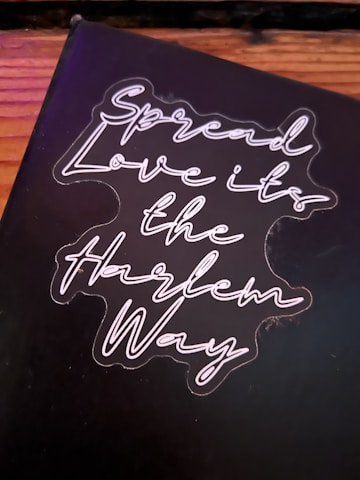 A black background with neon-style cursive text that reads 'Spread Love it's the Harlem Way'. The text is bright and stands out against the darker backdrop.