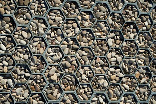 A collection of small, smooth stones arranged within hexagonal metal frames, creating a visually appealing geometric pattern. The stones vary in color from light beige to dark gray, adding a natural variation to the organized structure.