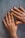 Two hands with decorated fingernails resting on a textured surface. The nails feature a design with black tips and small black dots on a nude base.