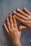 Two hands with decorated fingernails resting on a textured surface. The nails feature a design with black tips and small black dots on a nude base.
