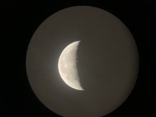A crescent moon is prominently visible against a dark background, with distinct craters and lunar surface details captured in the image.