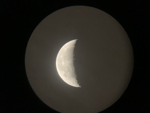 A crescent moon is prominently visible against a dark background, with distinct craters and lunar surface details captured in the image.