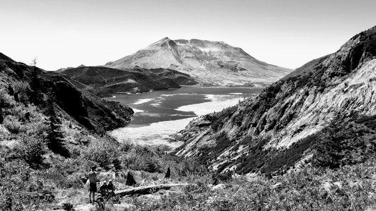 A scenic view of a traveler exploring a vast natural landscape with mountains and water.