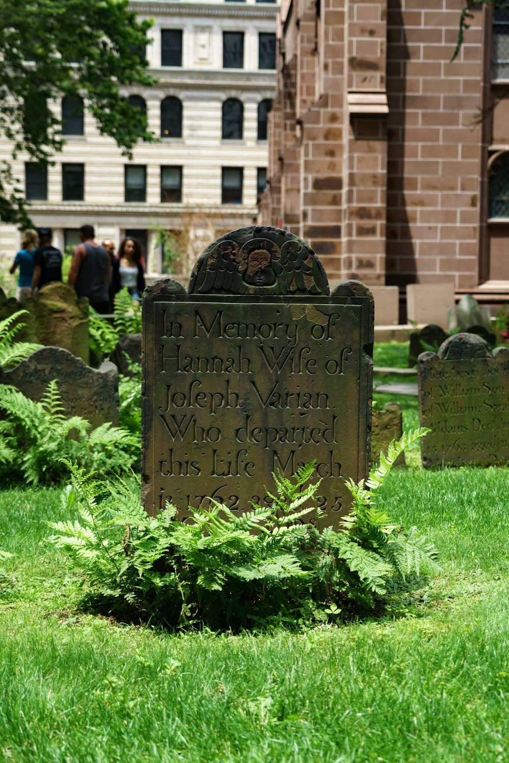 a stone with a face carved into it in a grassy area with people in the background