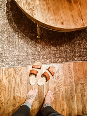 A close-up of a stylish tan sandal with intricate straps resting on a wooden bench.