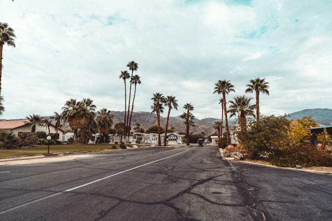 Quiet desert neighborhood street lined with palm trees and single-story homes with mountains in the distance