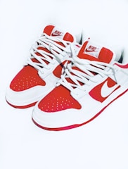 A pair of stylish sneakers with a bold red and white color scheme. The sneakers feature a prominent logo on the tongue and side, and are equipped with white laces.