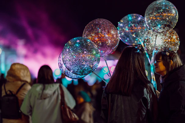 A festive scene with children and adults enjoying glitter and face painting under colorful event lights.