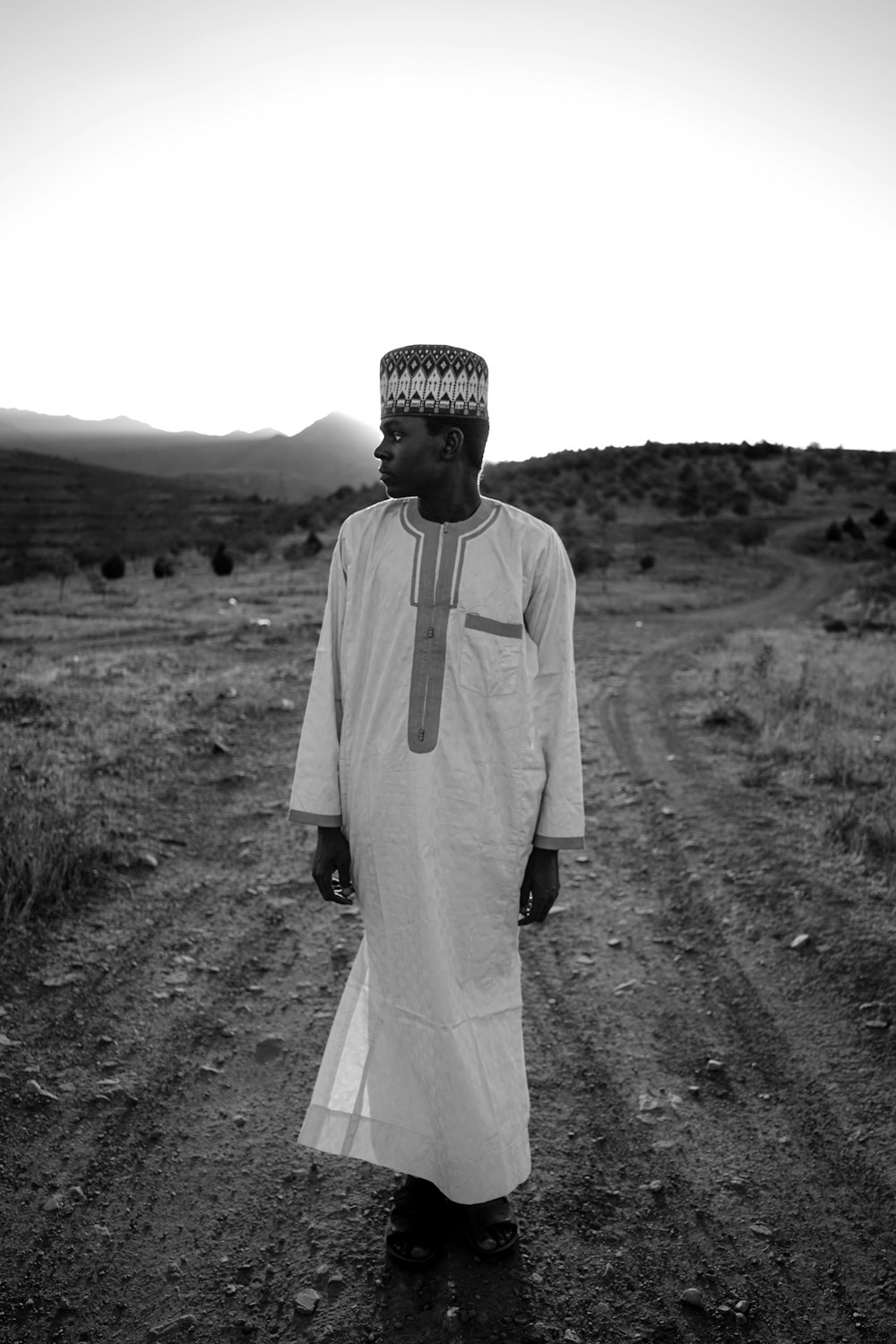 a man wearing a white robe and standing on a dirt road