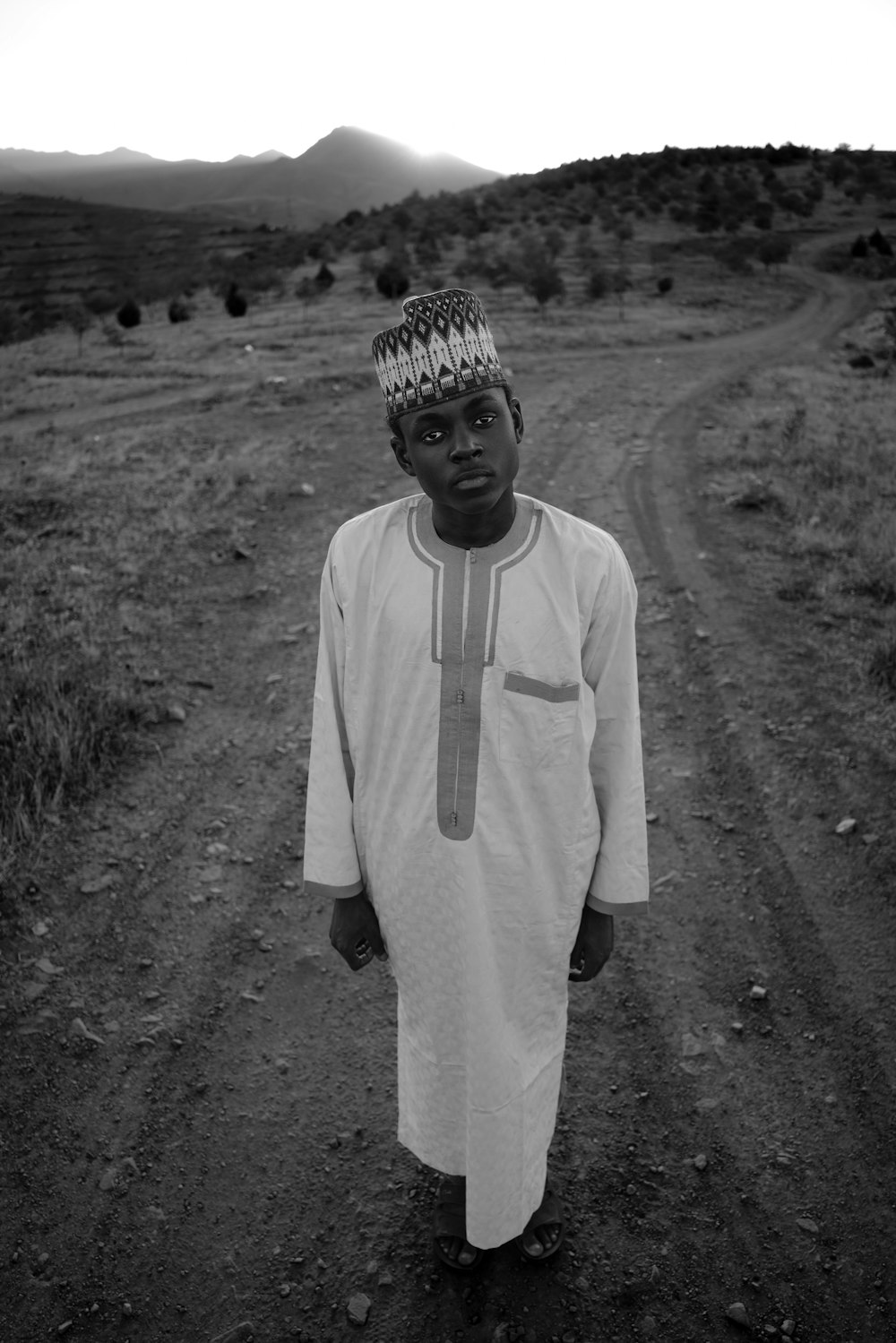 a young boy standing on a dirt road with hills in the background