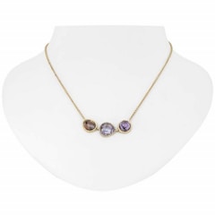 A gold necklace with three distinct gemstone pendants displayed on a white bust. The pendants include a brown, a clear, and a purple gemstone, each encased in a gold setting.