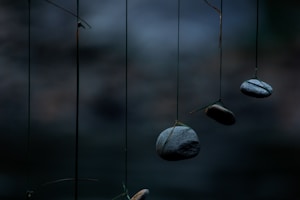 Several smooth stones are suspended by thin cords against a dark, blurred background. The stones appear to be balanced, creating a serene and minimalist composition.