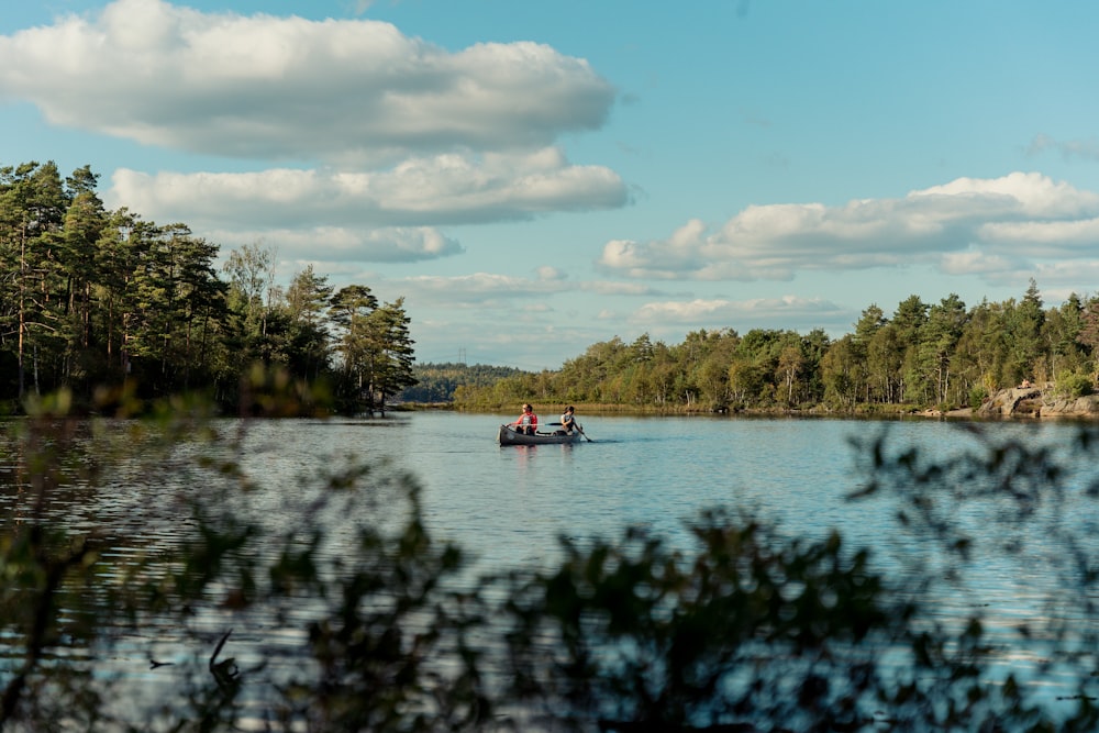 a couple people in a boat on a lake surrounded by trees
