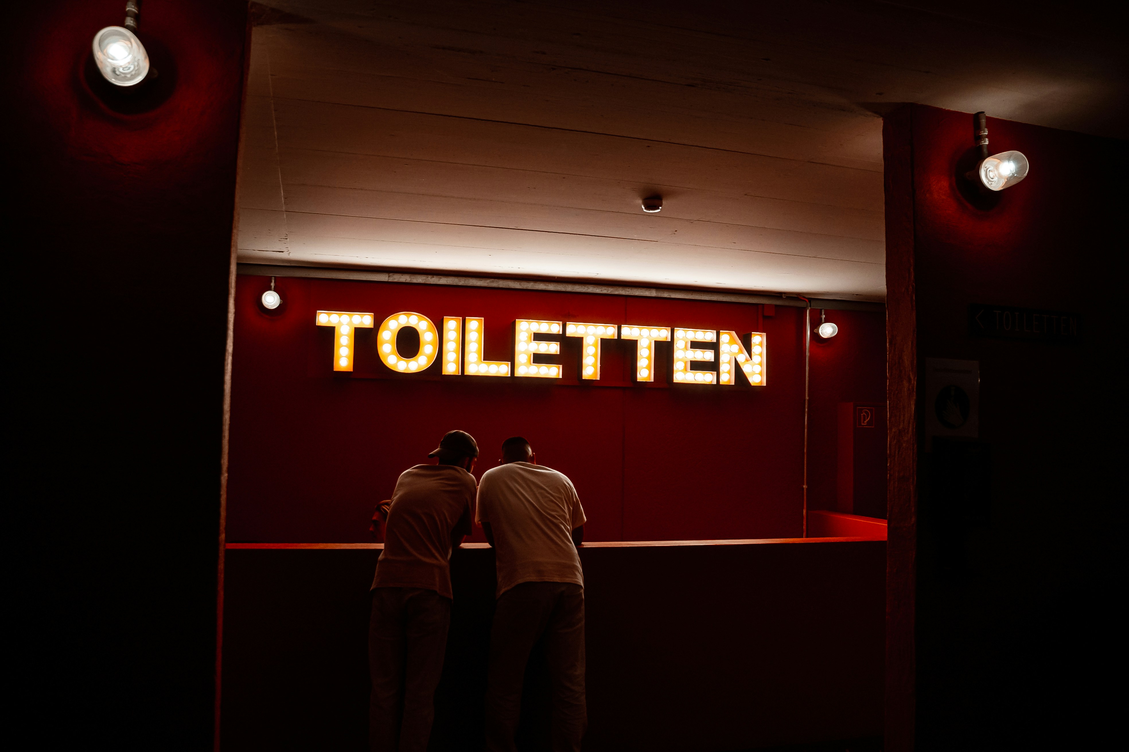 Un par de hombres parados frente a un letrero rojo con texto blanco