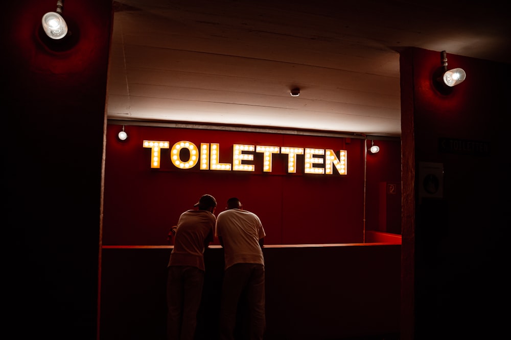 a couple of men standing in front of a red sign with white text