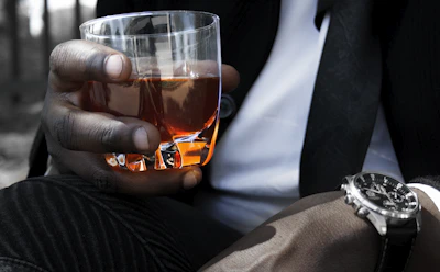 Close-up of a hand pouring amber whisky into a crystal glass on a rustic wooden table.