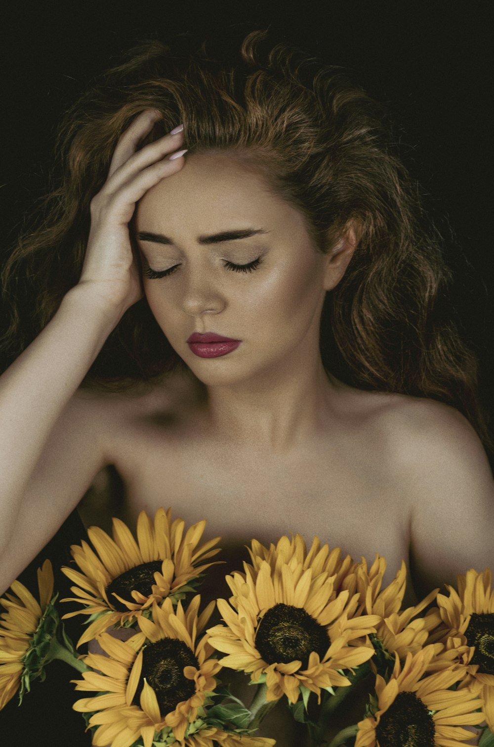 a woman with her hand on her face and sunflowers in the background