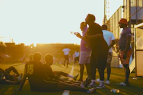 Group of friends celebrating a goal on an outdoor beach soccer field at sunset.