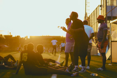 Group of friends celebrating a goal on an outdoor beach soccer field at sunset.