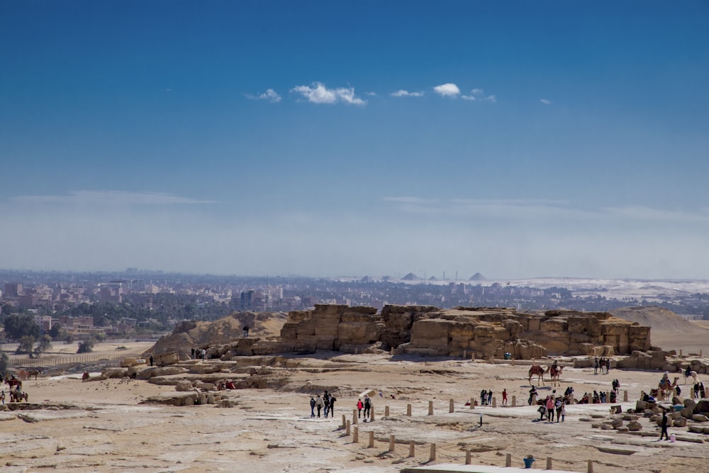 a large group of people on a sandy beach with a large rock formation in the background