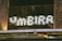 A sign reading 'FAMEIRA' in a dotted, illuminated style is mounted on a wooden and metallic structure. The letters are formed by bright white dots against a dark background, creating a striking contrast. The surrounding area shows weathered wood and some metal elements, suggesting an industrial or rustic setting.