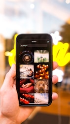 A hand holding a smartphone displaying various images related to religion. The images include crosses, candles, a person meditating, and architectural structures. The background is blurred with bright yellow lights.
