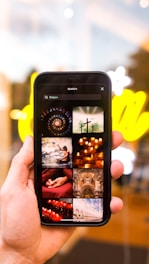 A hand holding a smartphone displaying various images related to religion. The images include crosses, candles, a person meditating, and architectural structures. The background is blurred with bright yellow lights.