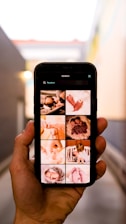 A hand is holding a smartphone displaying images related to newborns. The screen shows a grid of photos, including close-ups of baby feet, a baby wrapped in a blanket, and a baby being held by an adult. The background appears to be an alleyway with blurred walls and a light source visible.