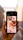 A hand is holding a smartphone displaying images related to newborns. The screen shows a grid of photos, including close-ups of baby feet, a baby wrapped in a blanket, and a baby being held by an adult. The background appears to be an alleyway with blurred walls and a light source visible.