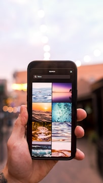 A person holds a smartphone displaying a search result for 'Water' with various images of water scenes, including waves, ripples, and splashes. The background is blurred with bokeh lights, suggesting an outdoor evening setting.