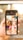 A person holds a smartphone displaying a search screen with the word 'Beauty' and a grid of various images. The images appear to showcase different aspects of beauty, such as portraits of women, close-ups, and artistic visuals. The background is blurred with warm lighting, suggesting an indoor or outdoor setting with sunlight.