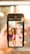 A person holds a smartphone displaying a search screen with the word 'Beauty' and a grid of various images. The images appear to showcase different aspects of beauty, such as portraits of women, close-ups, and artistic visuals. The background is blurred with warm lighting, suggesting an indoor or outdoor setting with sunlight.