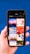 A hand holding a smartphone displaying a search for 'Holiday' with a grid of images. The images include a boat on water at sunset, a red abstract holiday theme, ocean waves, a Christmas tree design, beach chairs, a camera with travel accessories, festive lights, and holiday greenery on a blue background.