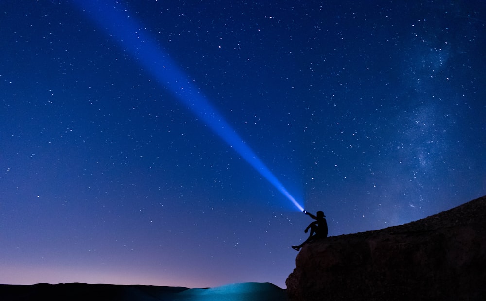 a person sitting on a rock with a bright light in the sky