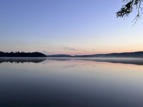 A tranquil Georgian lake at dawn with mist hovering over calm water.