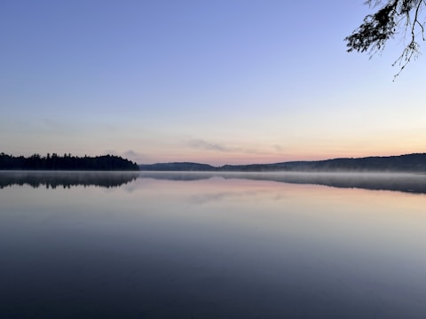 A peaceful lake at dawn with gentle mist and colorful sky reflections.