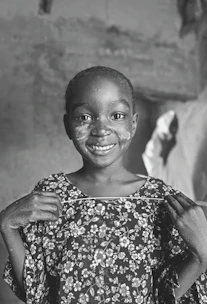 A child smiling while holding a colorful handmade card in a hospital room.