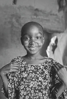 A smiling child holding a handmade card in a sunlit community center.