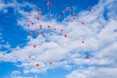Close-up of a single red heart-shaped balloon floating against a clear blue sky.