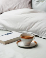 A melara max pillow placed on a stylish couch beside a steaming cup of tea and an open book.