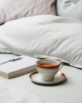 A warm cup of herbal tea resting on a bedside table next to a book.