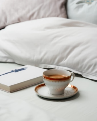 A cozy cup of steaming tea resting on a bedside table next to a softly glowing lamp and an open book.