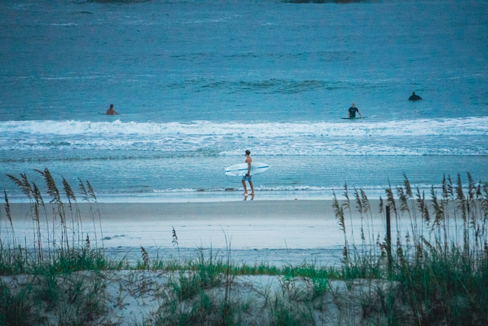 a couple of people walk across the beach with surfboards