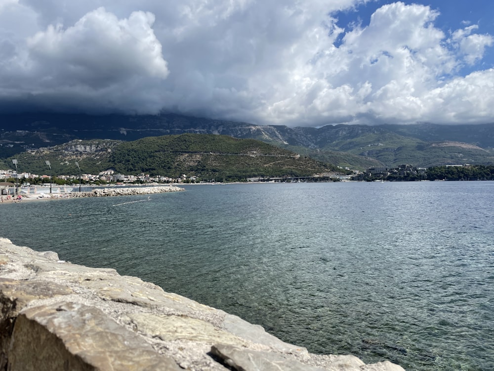 a body of water with a rocky shore and a hill in the background