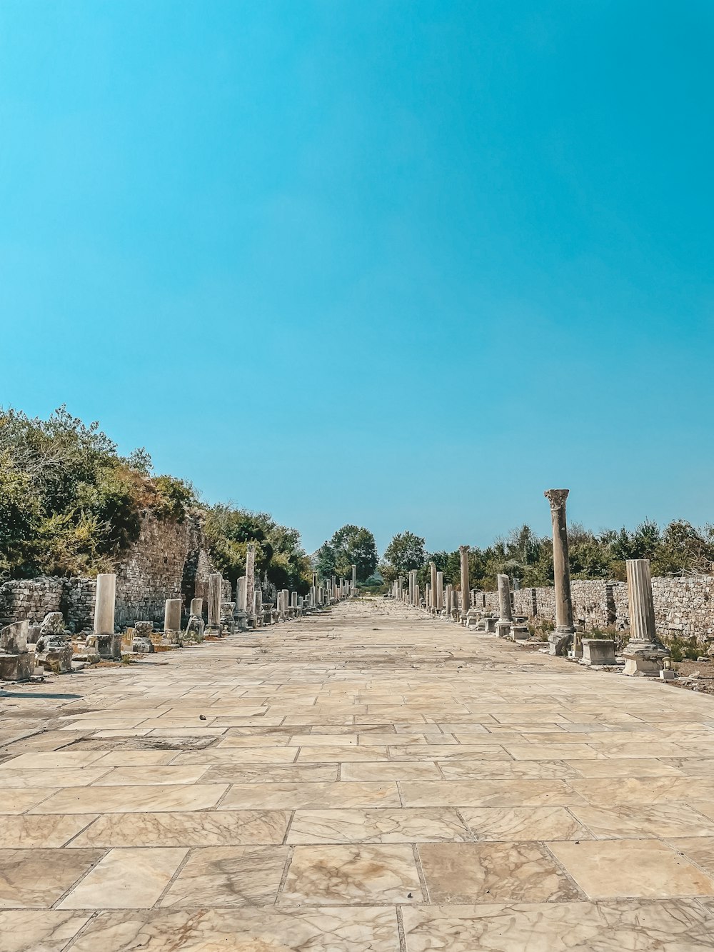 a stone walkway with a stone wall and trees on the side