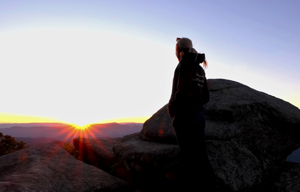 um homem de pé em uma rocha olhando para o pôr do sol