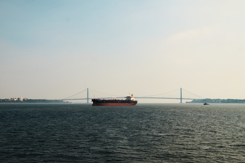 a large ship in the water with a bridge in the background