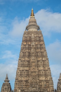 a tall building with a pointy top with Mahabodhi Temple in the background