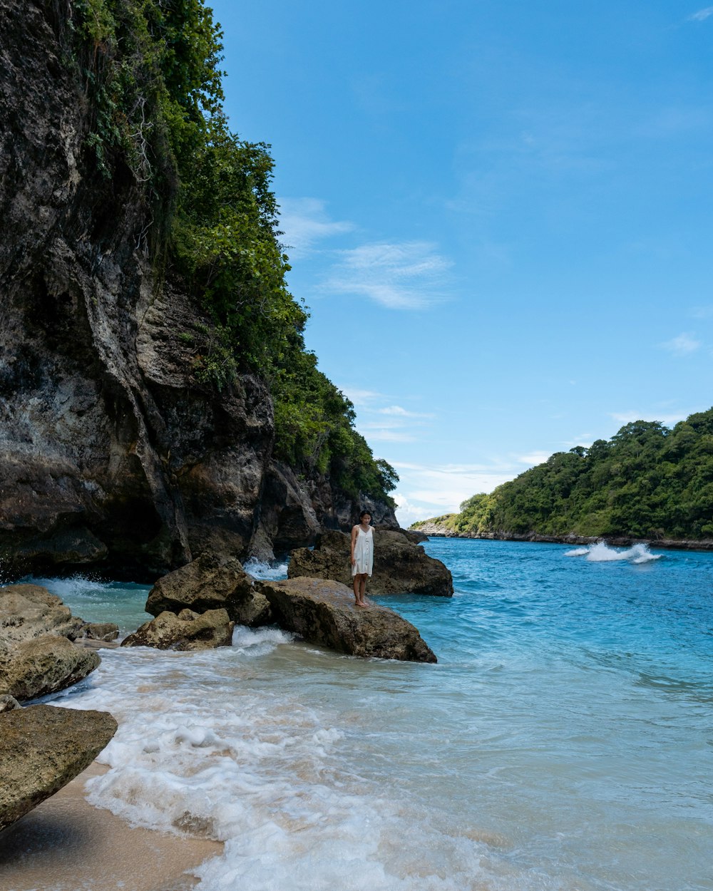 a person standing on a rock in the water by a beach